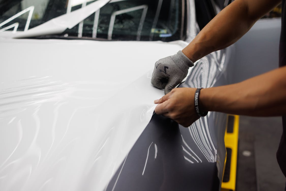 A person carefully applying a vinyl wrap to a car hood.