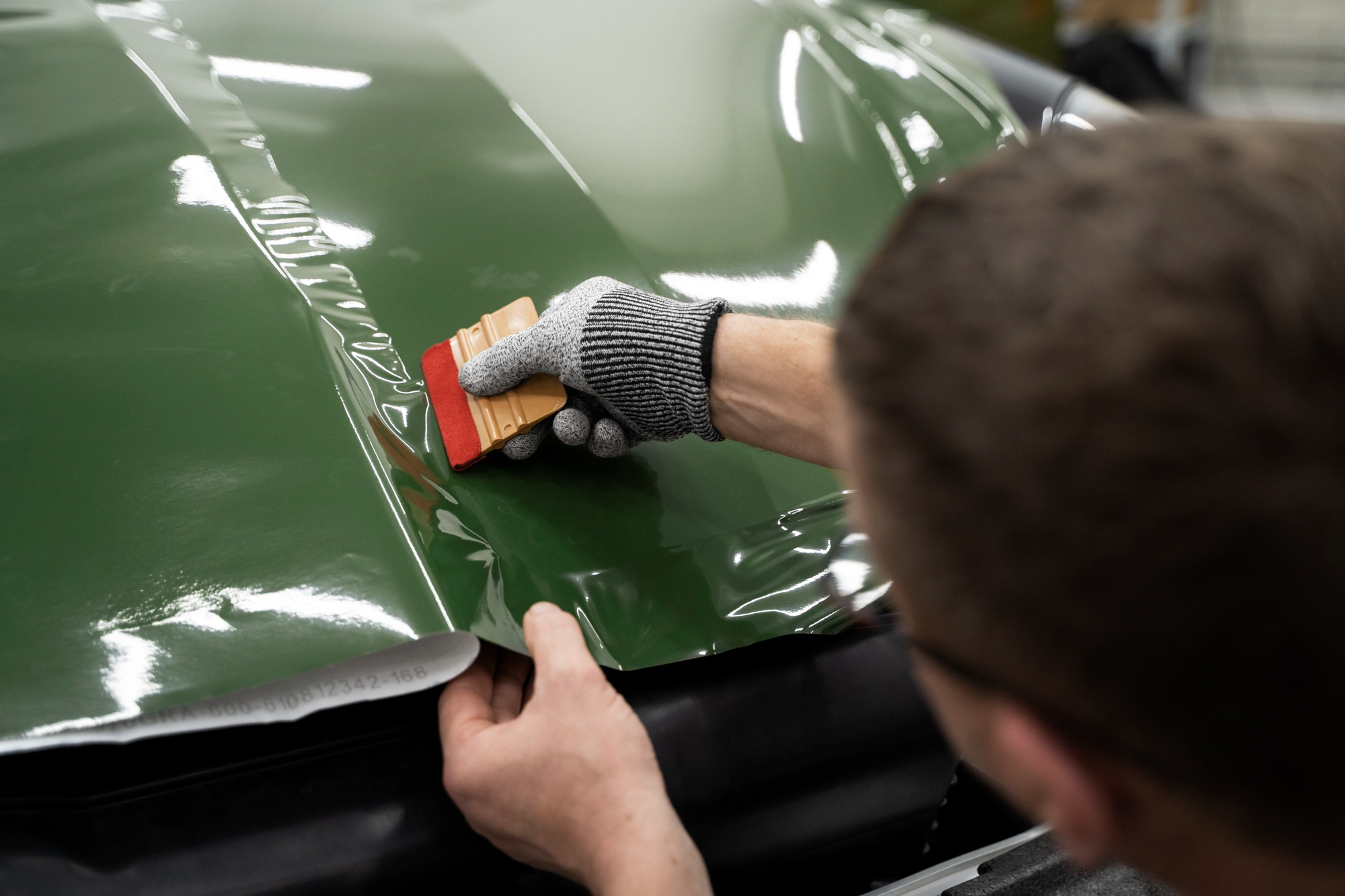 Technician installing car protection film on a vehicle to preserve its paint finish.
