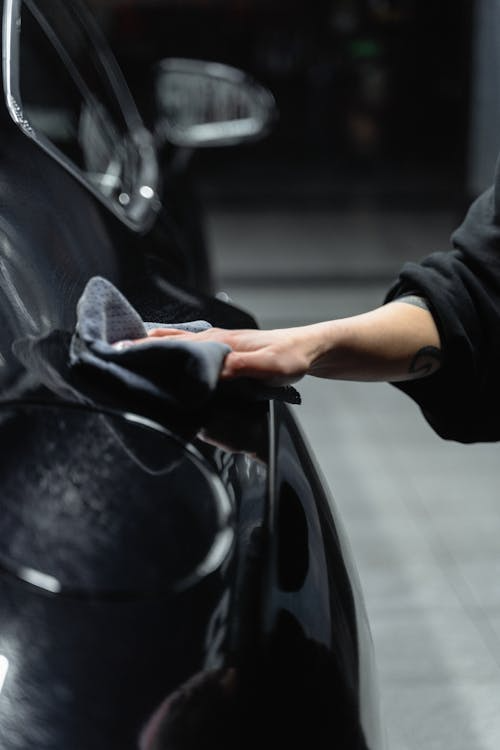 Person wiping a car surface with a microfiber cloth to prepare for applying paint protection film.