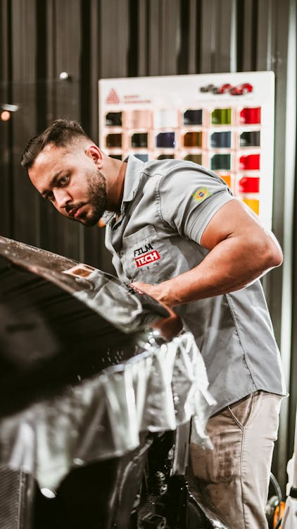 Bearded man carefully applying paint protection film on a car surface.