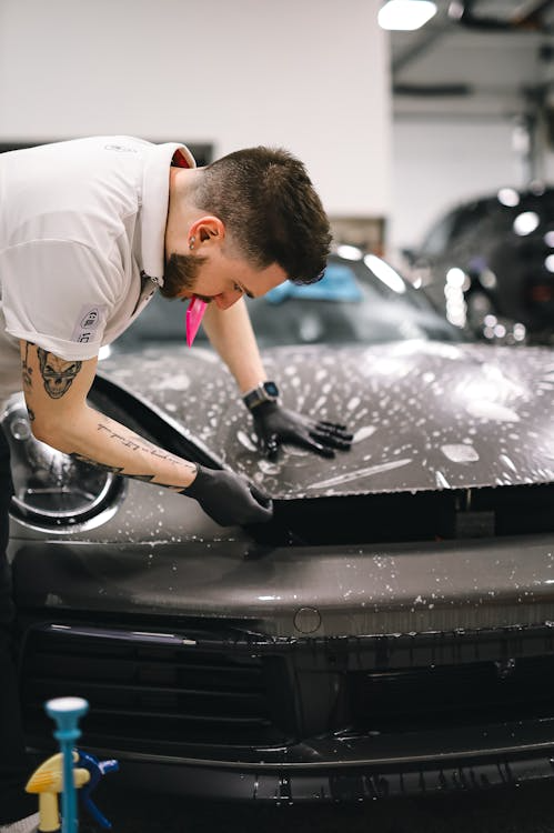 Bearded man applying paint protection film on a red sports car hood.