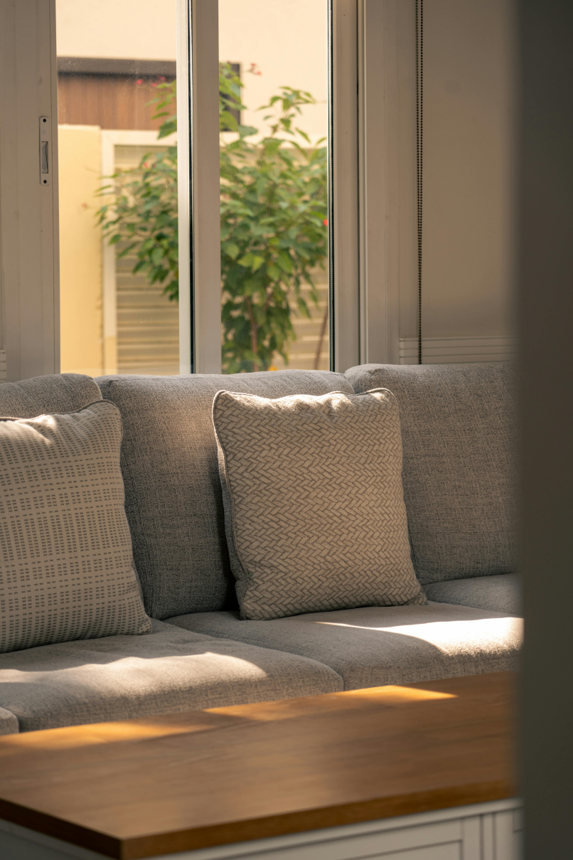 A cozy living room with a bright sofa and sunlight filtering through a window treated with solar control film, showing reduced glare.