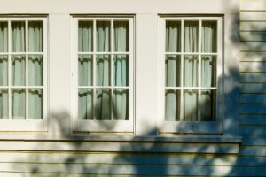 Front exterior of a house with window film on tall curtained windows framed in white trim.