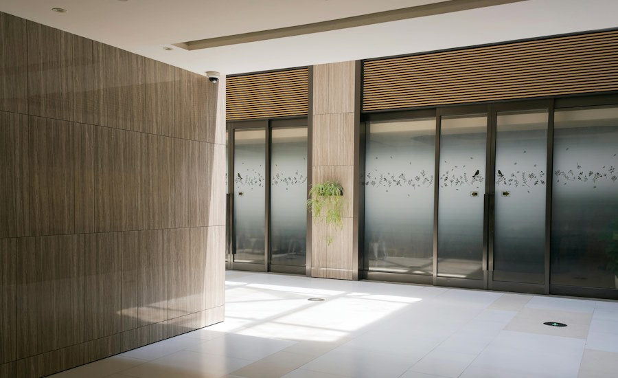 decorative frosted glass film modern lobby Bright modern lobby with wood wall panelling, frosted glass doors, and subtle botanical bird-pattern detailing across the glass.