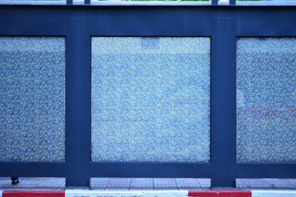 Blue-framed privacy glass panels along a streetfront façade with textured translucent surfaces and sidewalk below.